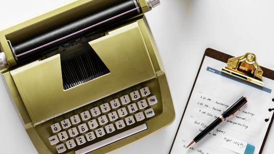 Gold typewriter on left and a sheet of paper on a pad with pen on right