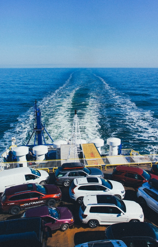 vehicles on a cargo ship with wake of the ship in the background