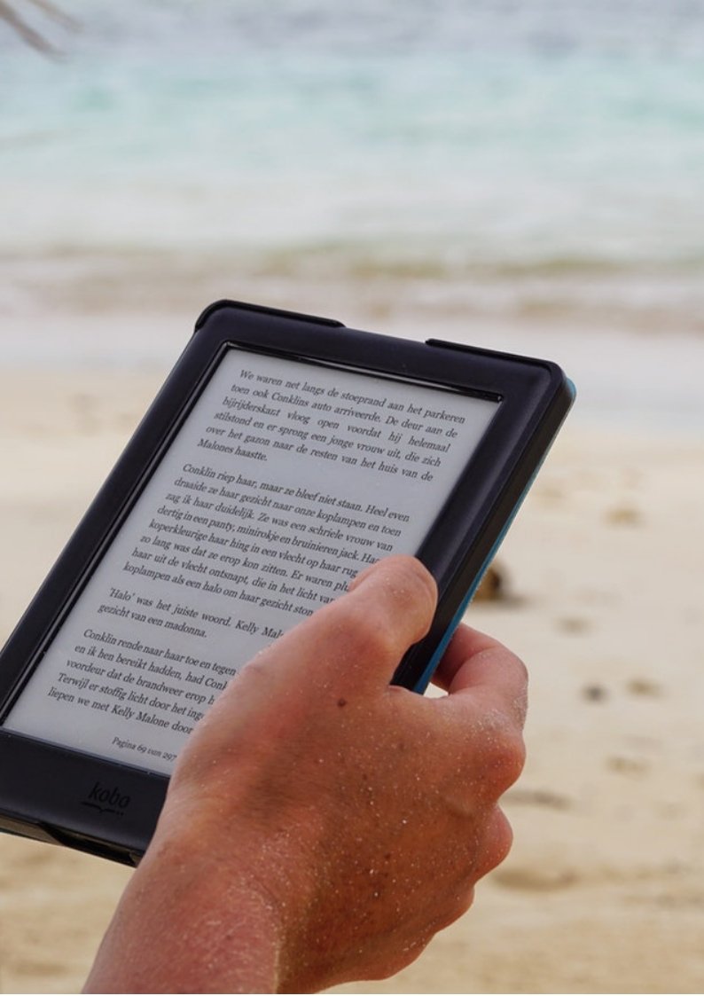 An image of a hand holding a tablet with beach background 