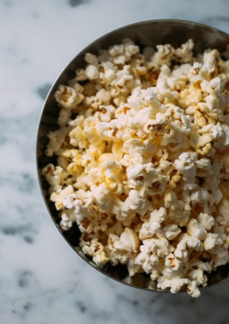 An image of a black bowl with popcorn in it placed at a white surface 