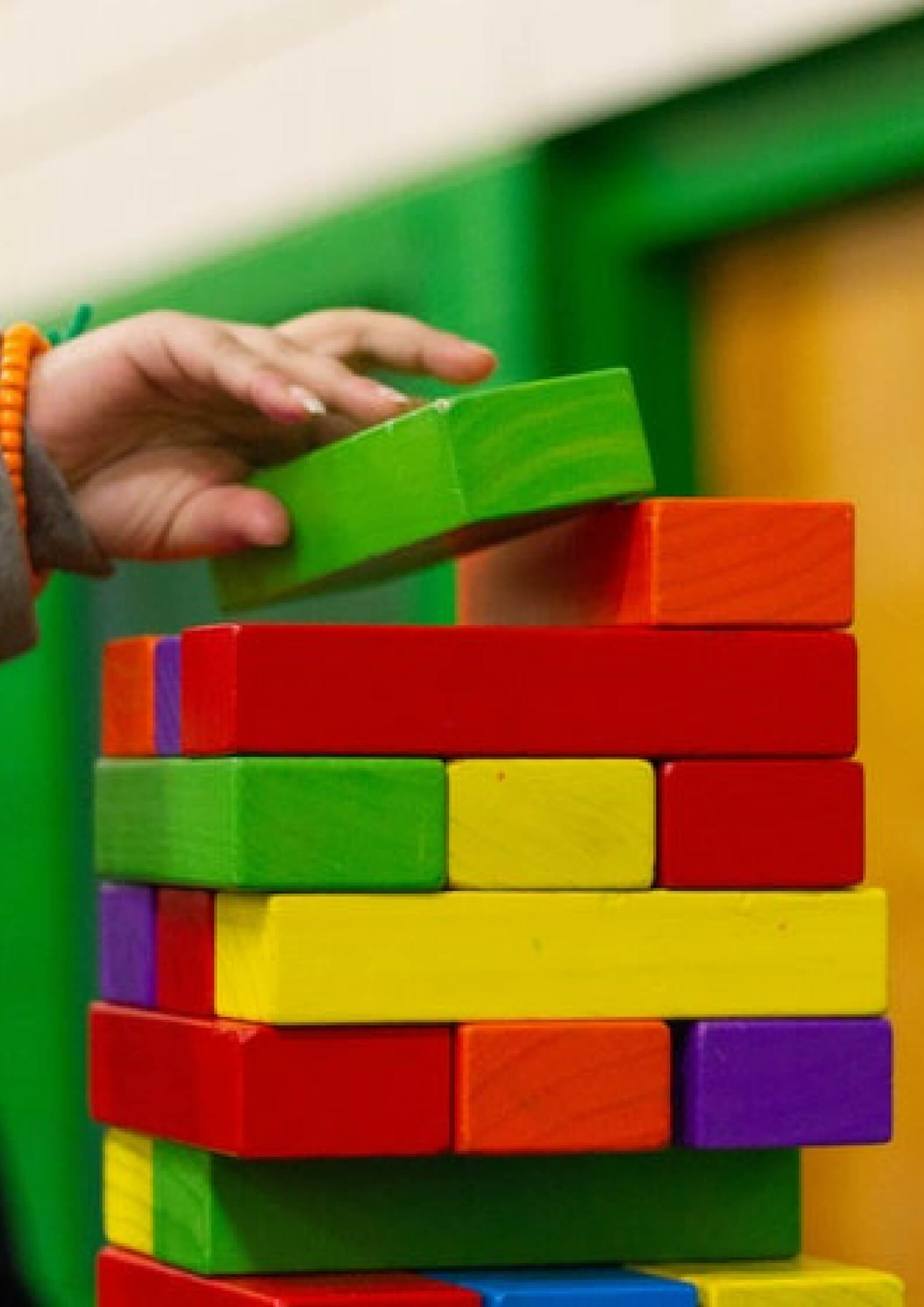 Image of child's hand placing green block on a well defined building that is constructed by other color blocks.