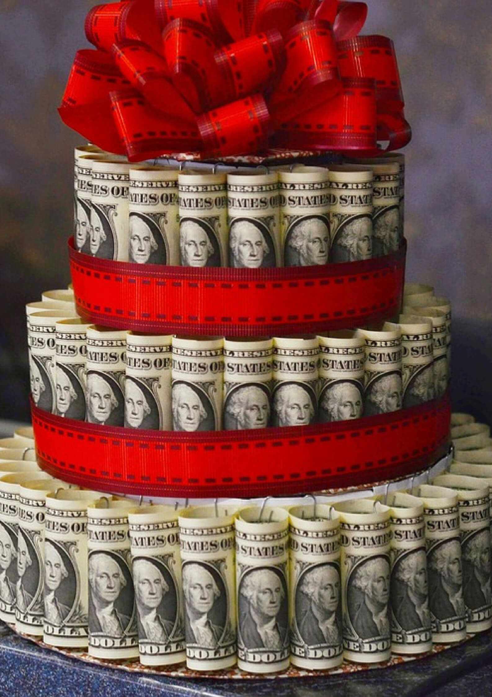 Image of European currency made in shape of a three layered cake with red bow on the top 