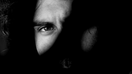 Black and white photo of a man's face with one eye visible and one eye hidden behind shadow