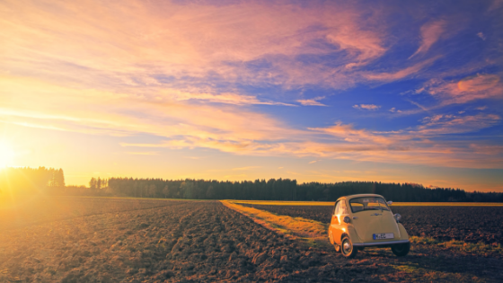a car parked in an open field with sun setting in the distance