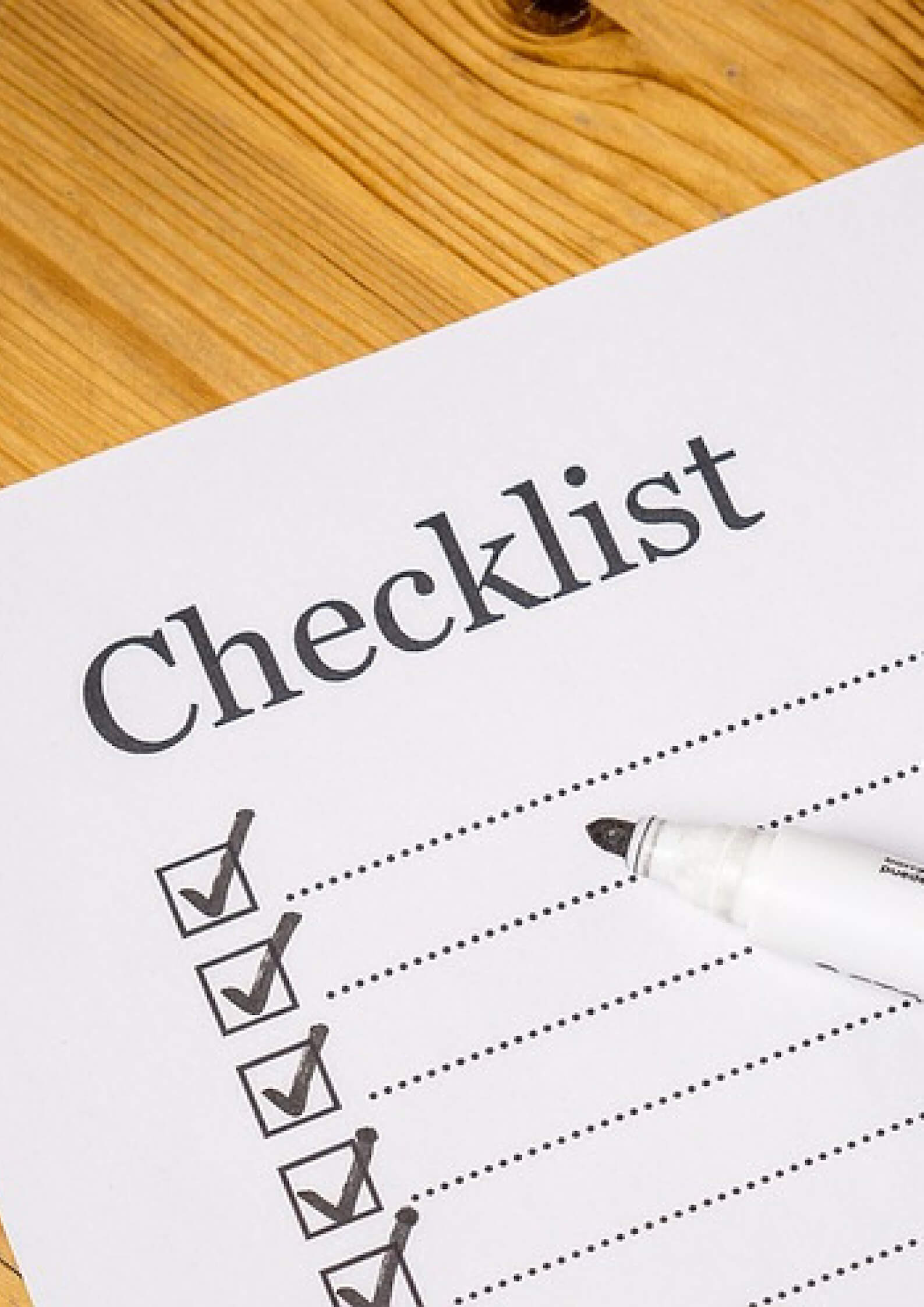 Image of a sheet which say checklist with a marker placed on a wooden board 