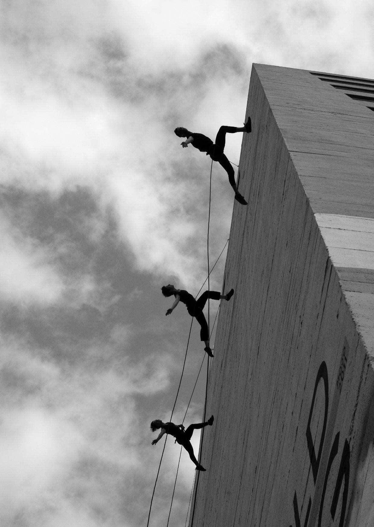 Three people can be seen climbing a wall on a single rope.