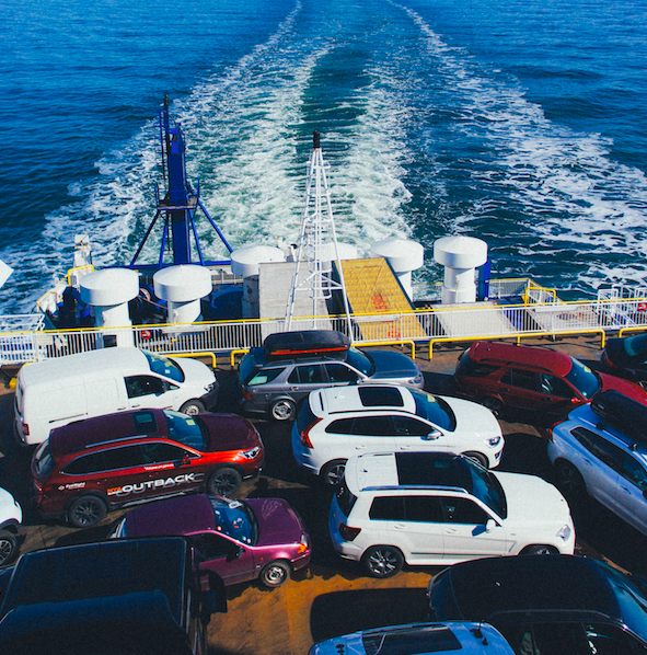 vehicles on a cargo ship with wake of the ship in the background