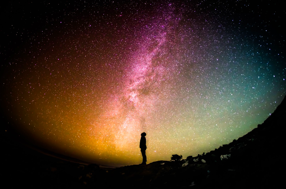 A man standing at night time under an open sky full of stars