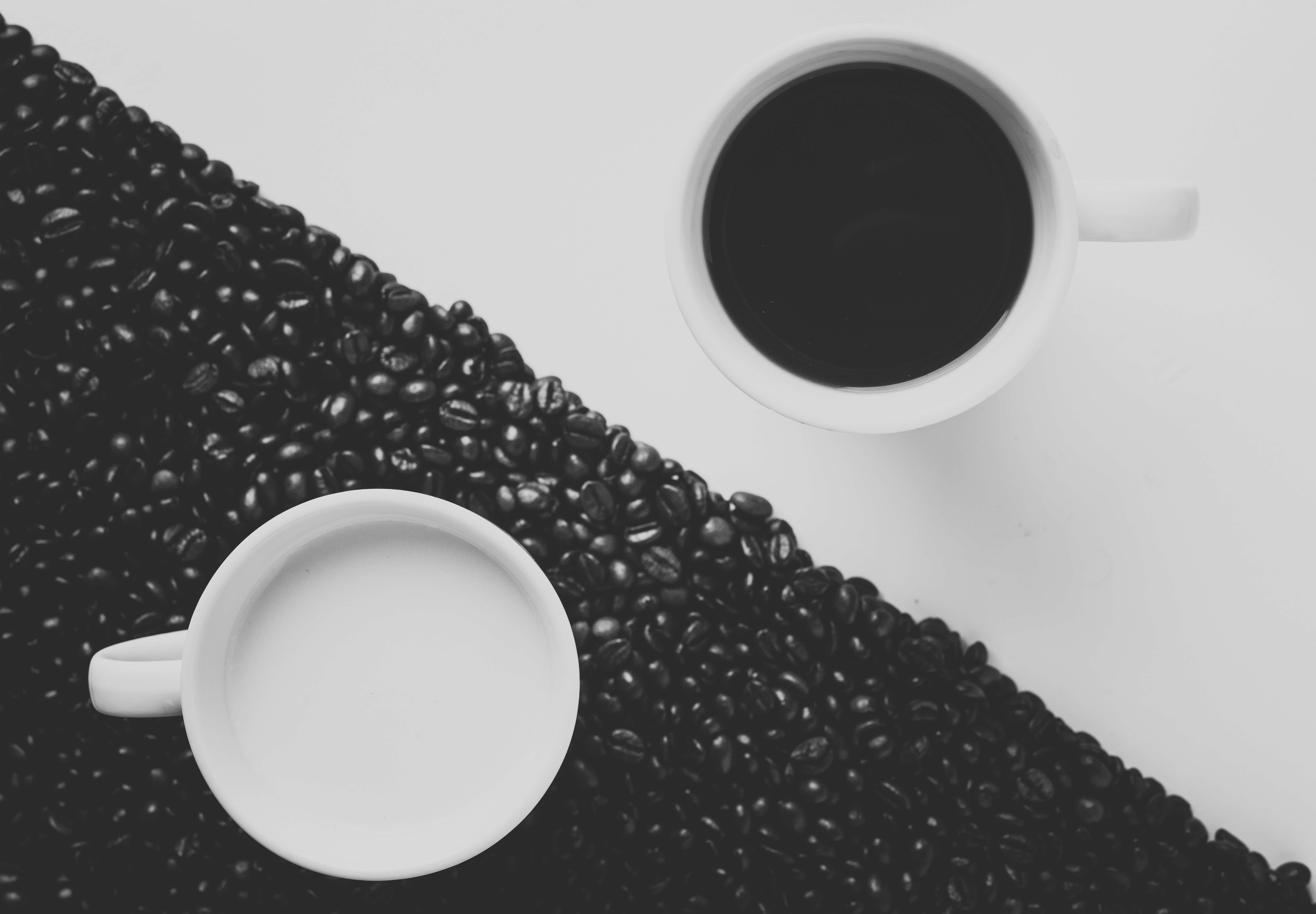 Two coffee mugs placed diagonally opposite to each other and coffee beans scattered around one of the mugs