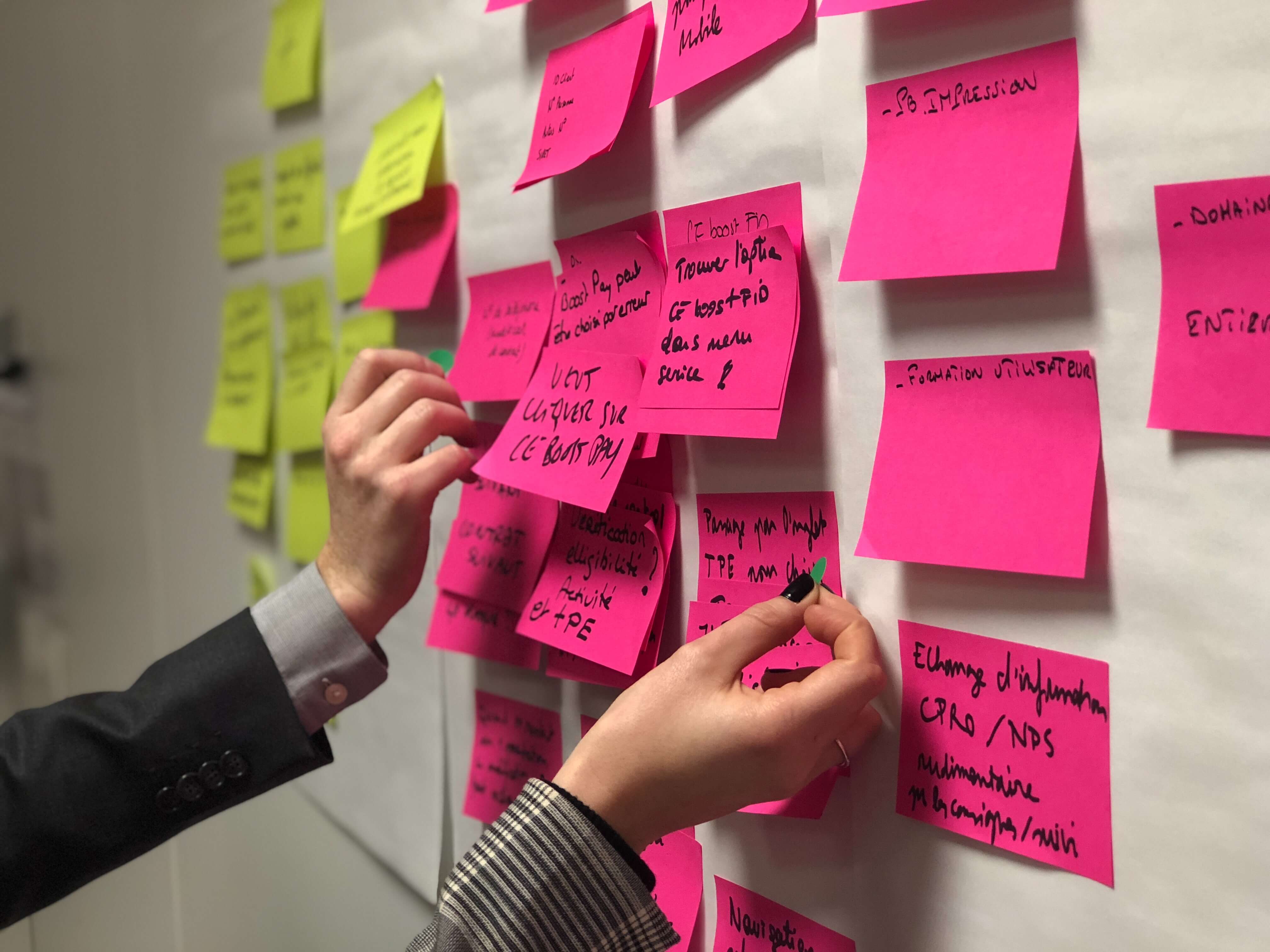Person holding pink and yellow sticky notes on a board