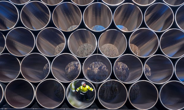 Front view of lots of hollow cylindrical pipes stacked on top of each other with a man sitting inside one of the pipes