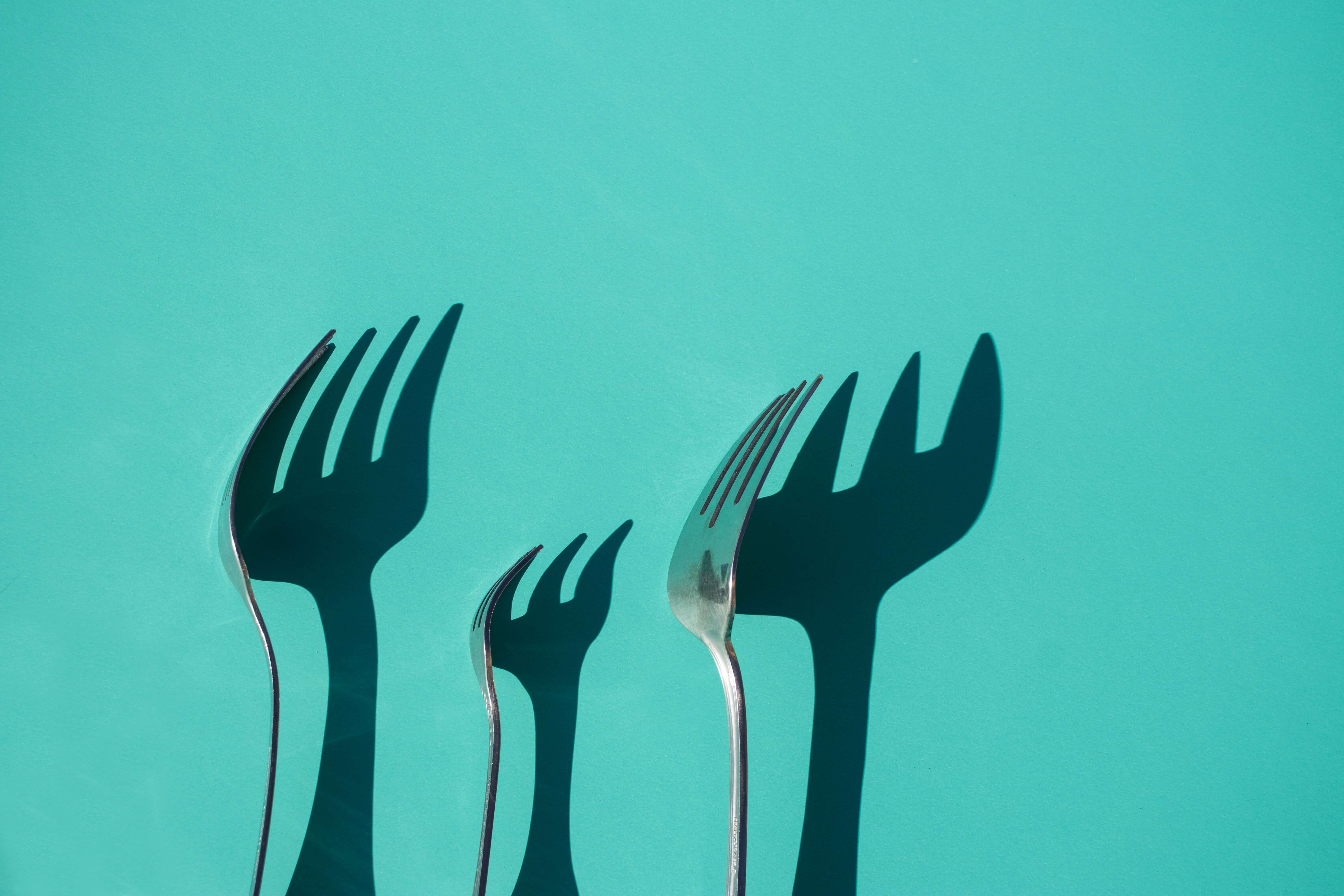 Three forks and their shadows falling on a green background