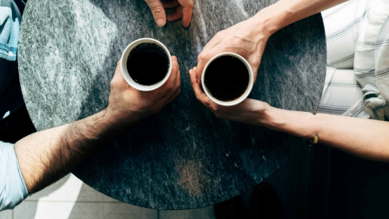 two people sitting opposite to each other holding each other's cup of coffee