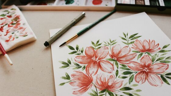 illustration image showing floral design on sketchbooks and brush and pen are placed on a brown desk 