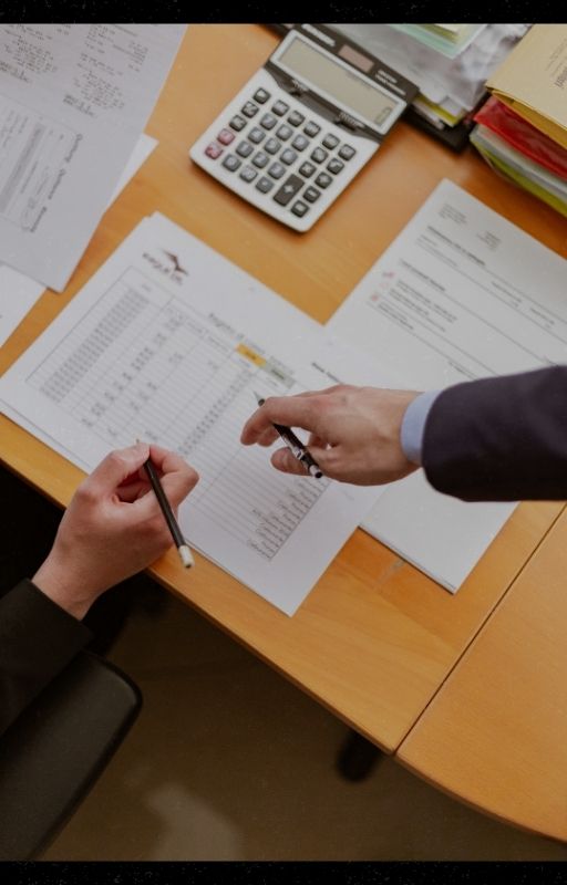 brown desk with papers and two hands pointing at it