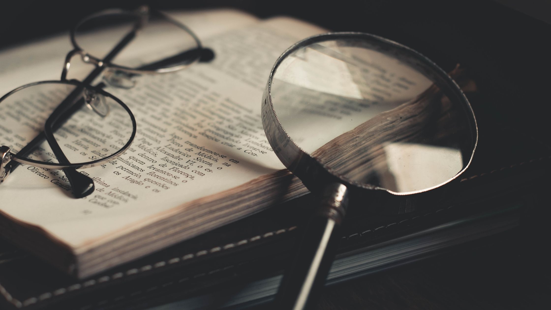 An open book, a pair of glasses and a magnifying glass can be seen kept together.