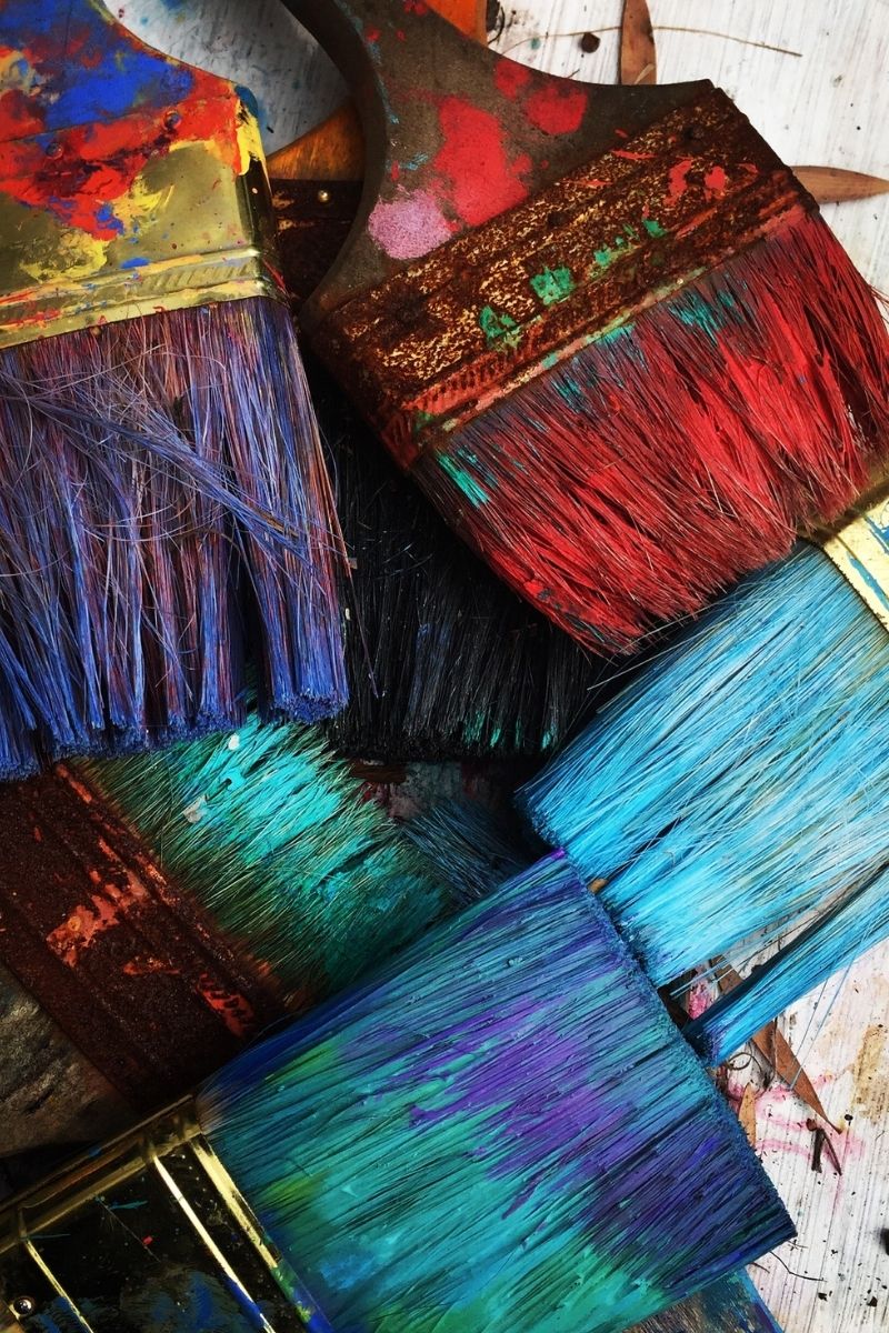A bunch of paint brushes are seen with colour on them.