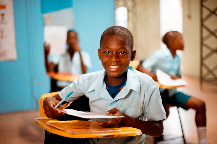 A student in the front and two behind him sitting on their chairs with a paper and a pen in their hands