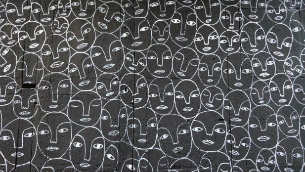 Illustartaion image showing repetitive human faces with eyes, nose, and lips were drawn in white colour on a grey background wall