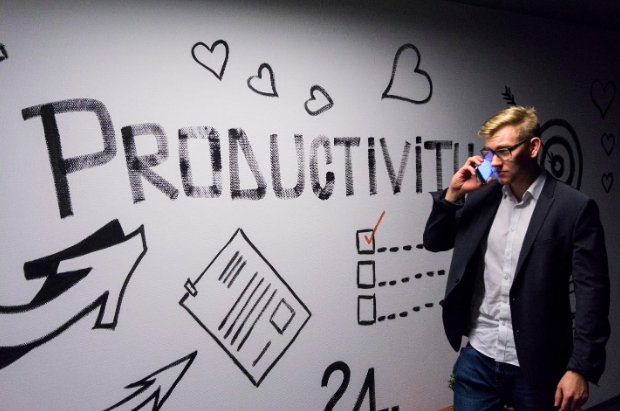 A guy talking on phone with a digital signage board displaying the word 'productivity' to represent benefits of Agile and lean for personal productivity