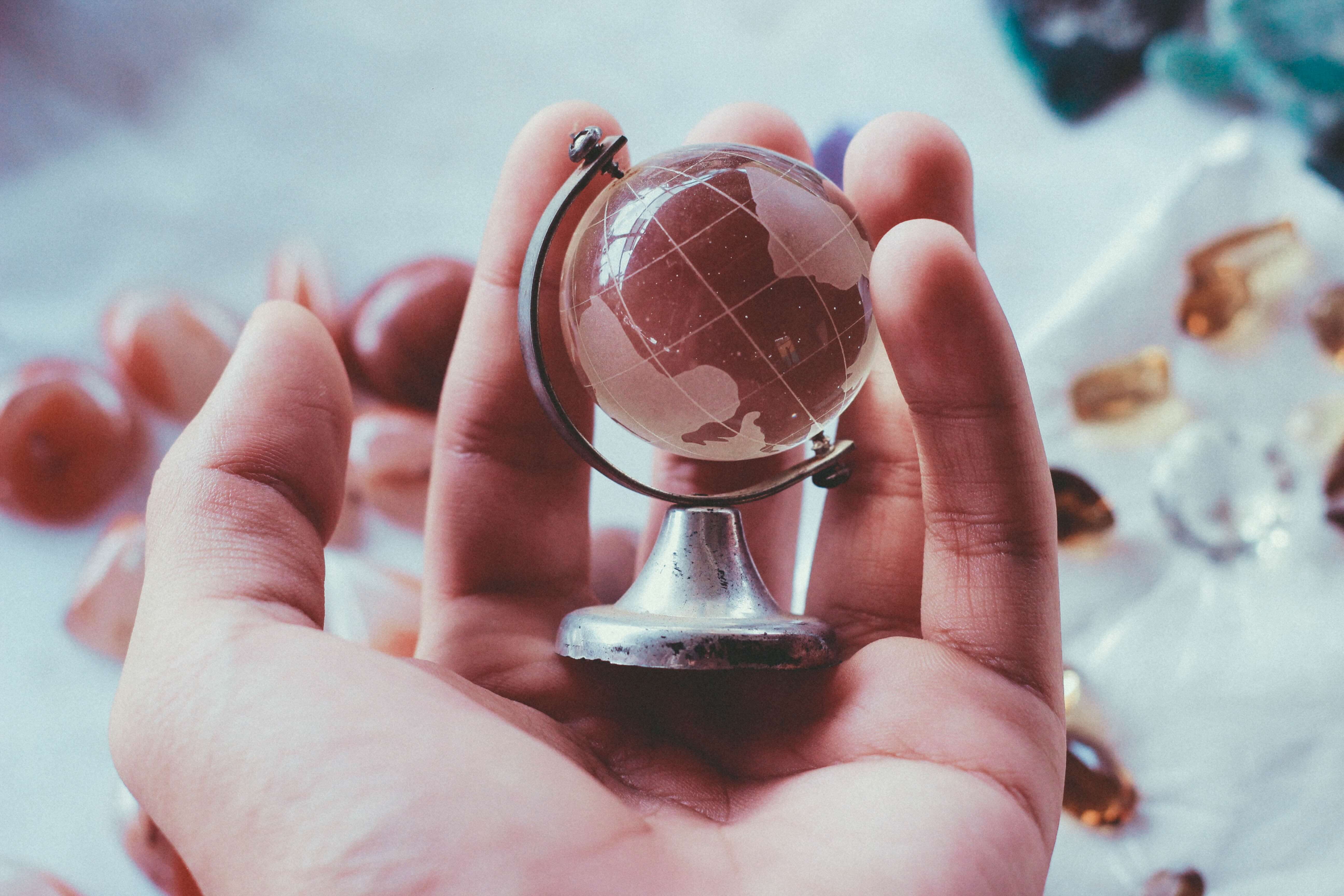 person holding grey metal framed desk globe paper weight