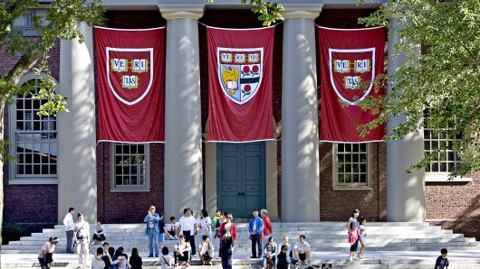 Building entrance with people sitting on stairs and three Harvard flags tucked on four pillars