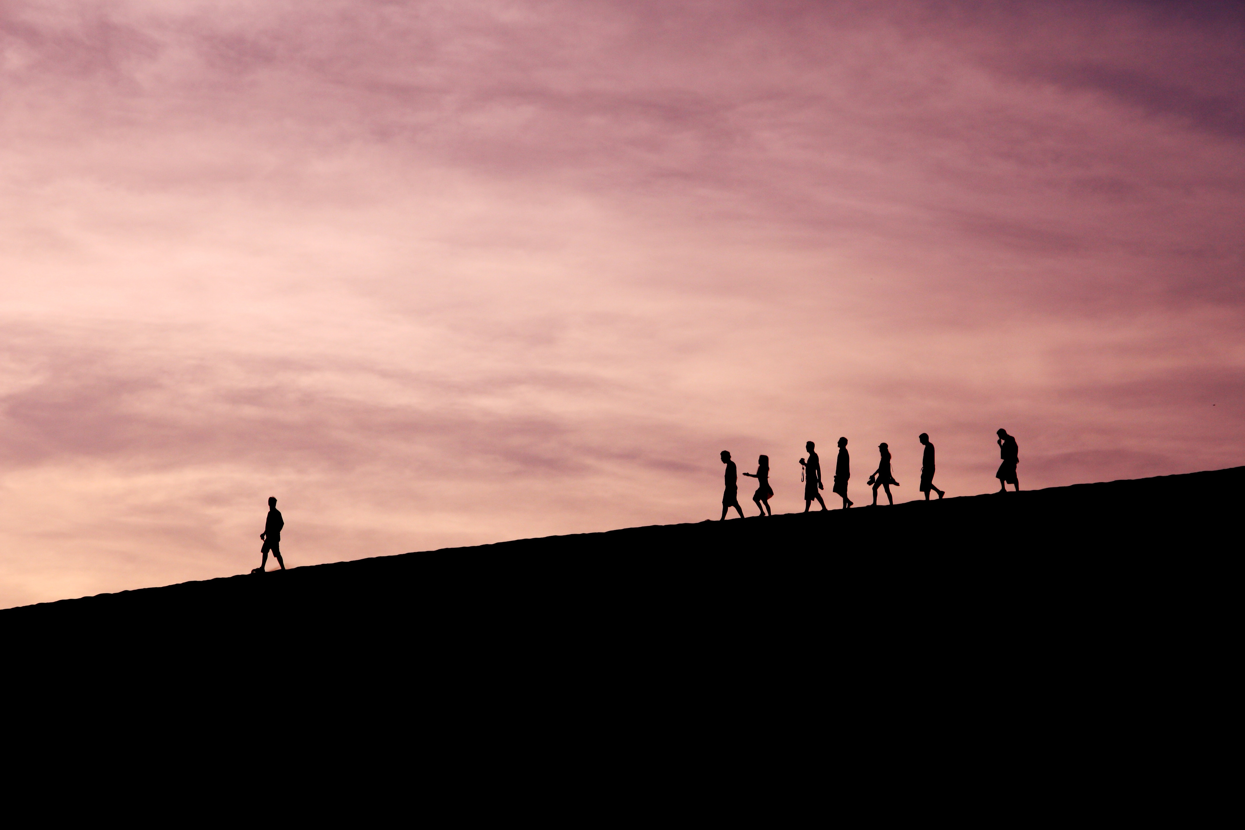 Dusky sky with people walking on a mountainous surface at a distance