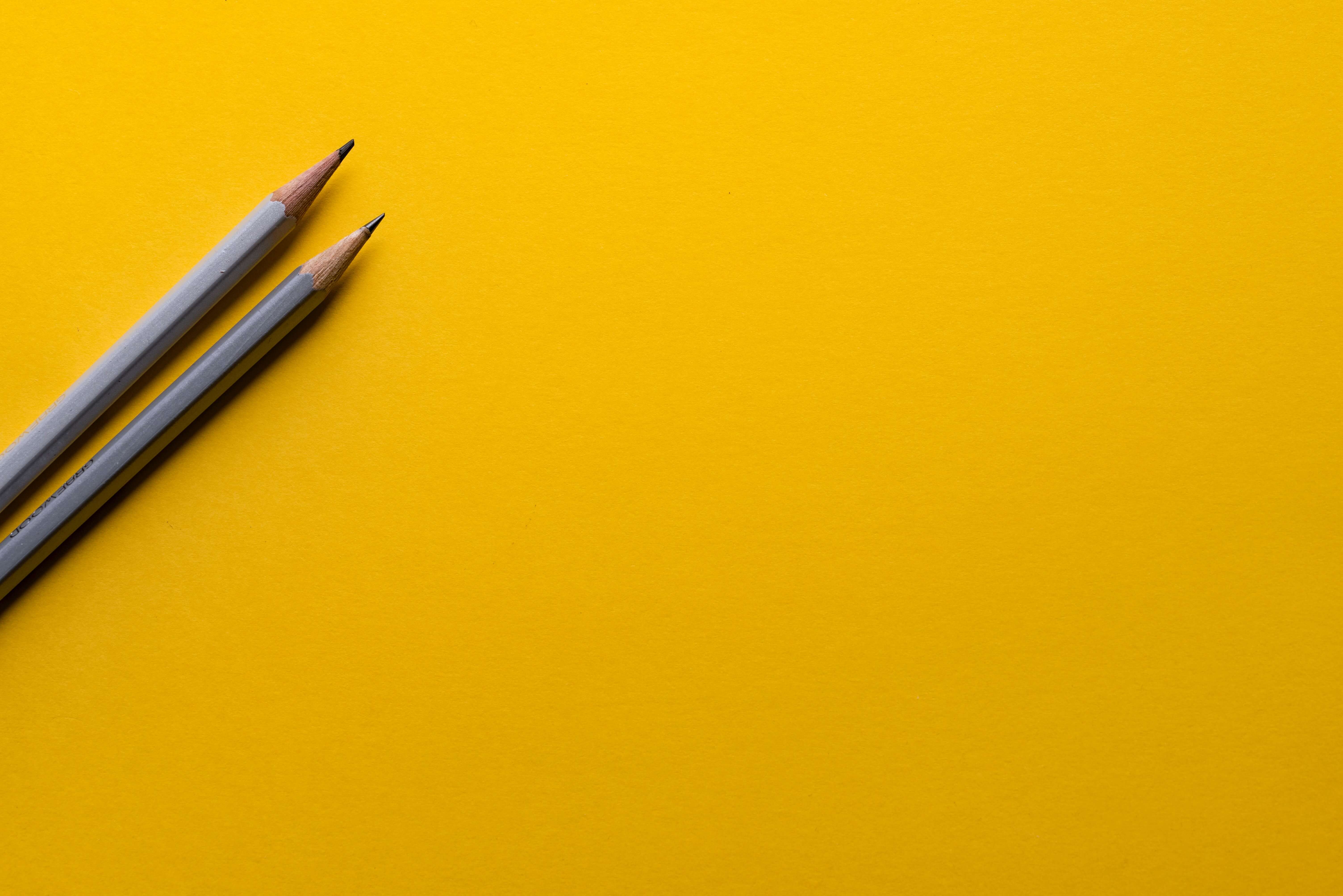 Two pencils placed over a yellowish surface to signify design briefs