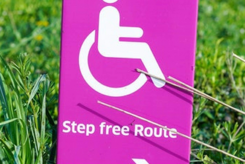 Image of a stick man sitting on a wheel chair with arrow sign below it in a pink background 