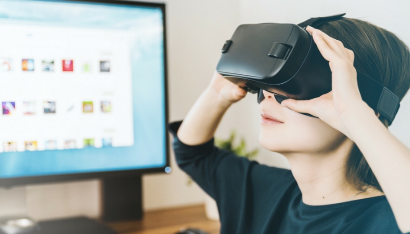 blog image with a girl wearing a VR headset besides a computer