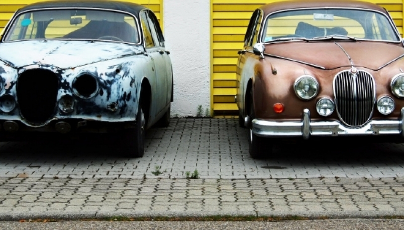one grey vintage car on left and one brown vintage car on right