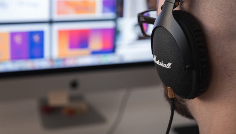 over the shoulder shot of a person with black headphones looking at the computer screen