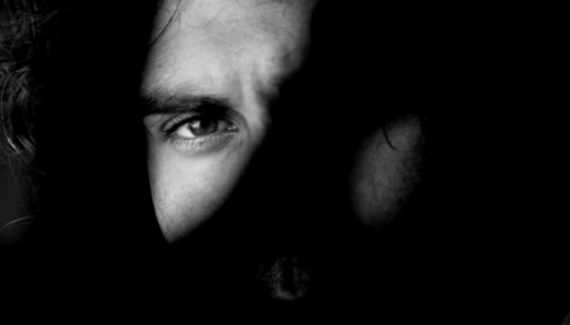Black and white photo of a man's face with one eye visible and one eye hidden behind shadow