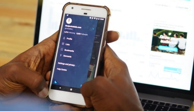 Image of hand holding a phone and a laptop is placed as a background 