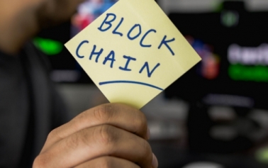 a hand holding a stick note with the word blockchain on it