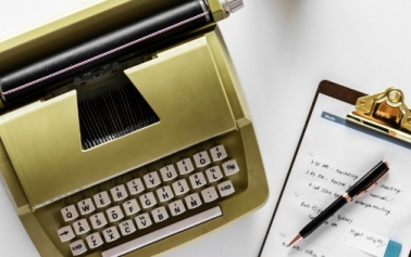 Gold typewriter on left and a sheet of paper on a pad with pen on right