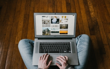 A person sitting with a laptop on their lap on a wooden floor 