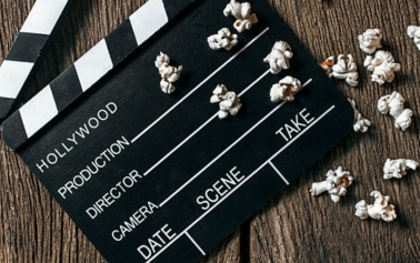 An image of a clapper board placed on a wooden surface with 19 popcorns positioned at the bottom of the clapper board 