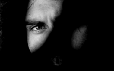 Black and white photo of a man's face with one eye visible and one eye hidden behind shadow
