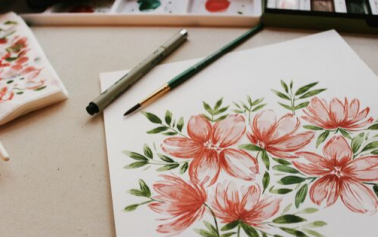 illustration image showing floral design on sketchbooks and brush and pen are placed on a brown desk 