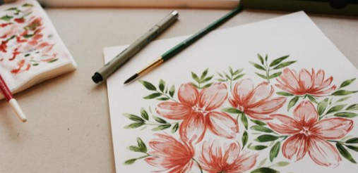 illustration image showing floral design on sketchbooks and brush and pen are placed on a brown desk