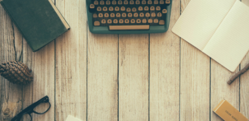 typewriter, notebook, specs, pine and other stationary on a wooden table