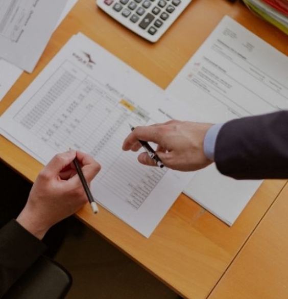 brown desk with papers and two hands pointing at it