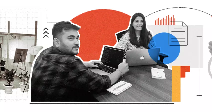 a boy and a girl sitting with laptop and looking towards the camera 