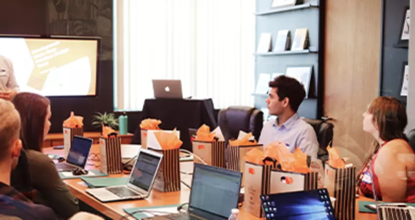 group of people sitting with laptops and a person is standing and explaining.