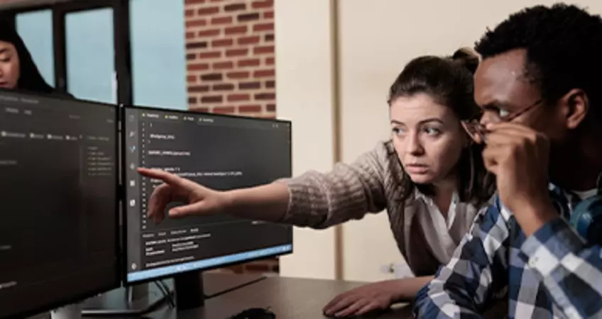 two people looking at computer screen and a woman seen behind the computer screen